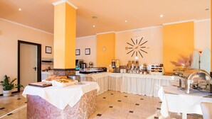 Ein Frühstücksbereich in einem Hotel mit einem reichhaltigen Buffet, einer Wanduhr und einer Tür links.