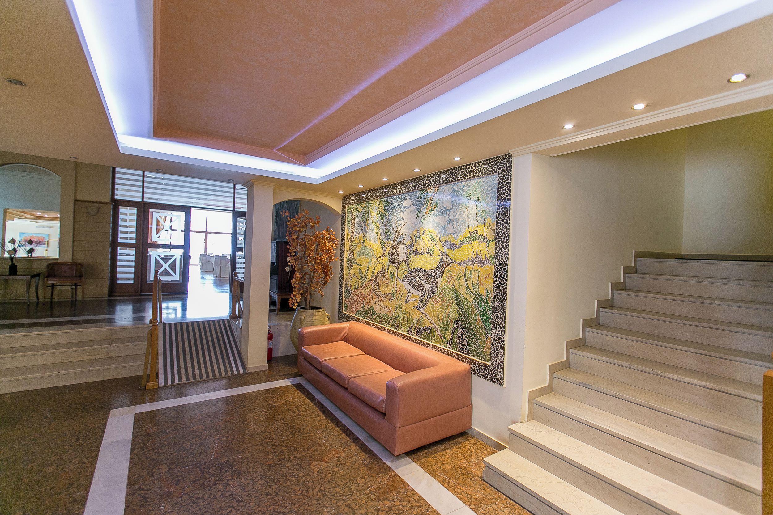 A lobby with a staircase, a large mosaic wall, and a sofa.