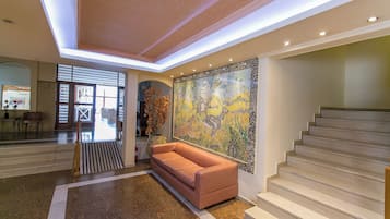A lobby with a staircase, a large mosaic wall, and a sofa.