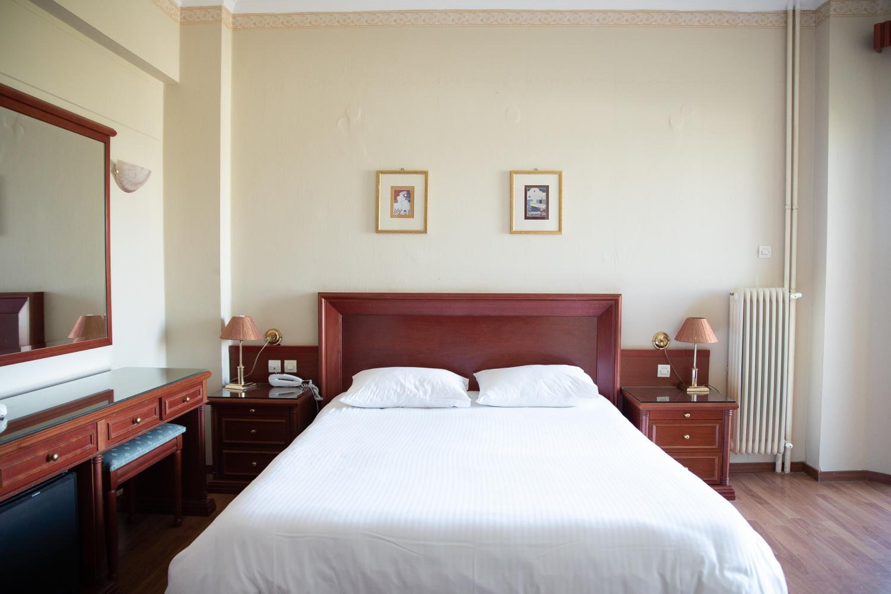 Habitación de hotel con una cama grande, un aparador de madera, un escritorio y dos cuadros en la pared.