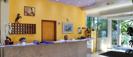 A reception desk with a receptionist, a wooden panel wall, a framed picture, and a door.
