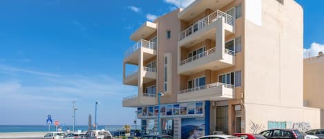 A multi-story building with balconies, a parking lot, and a view of the sea.