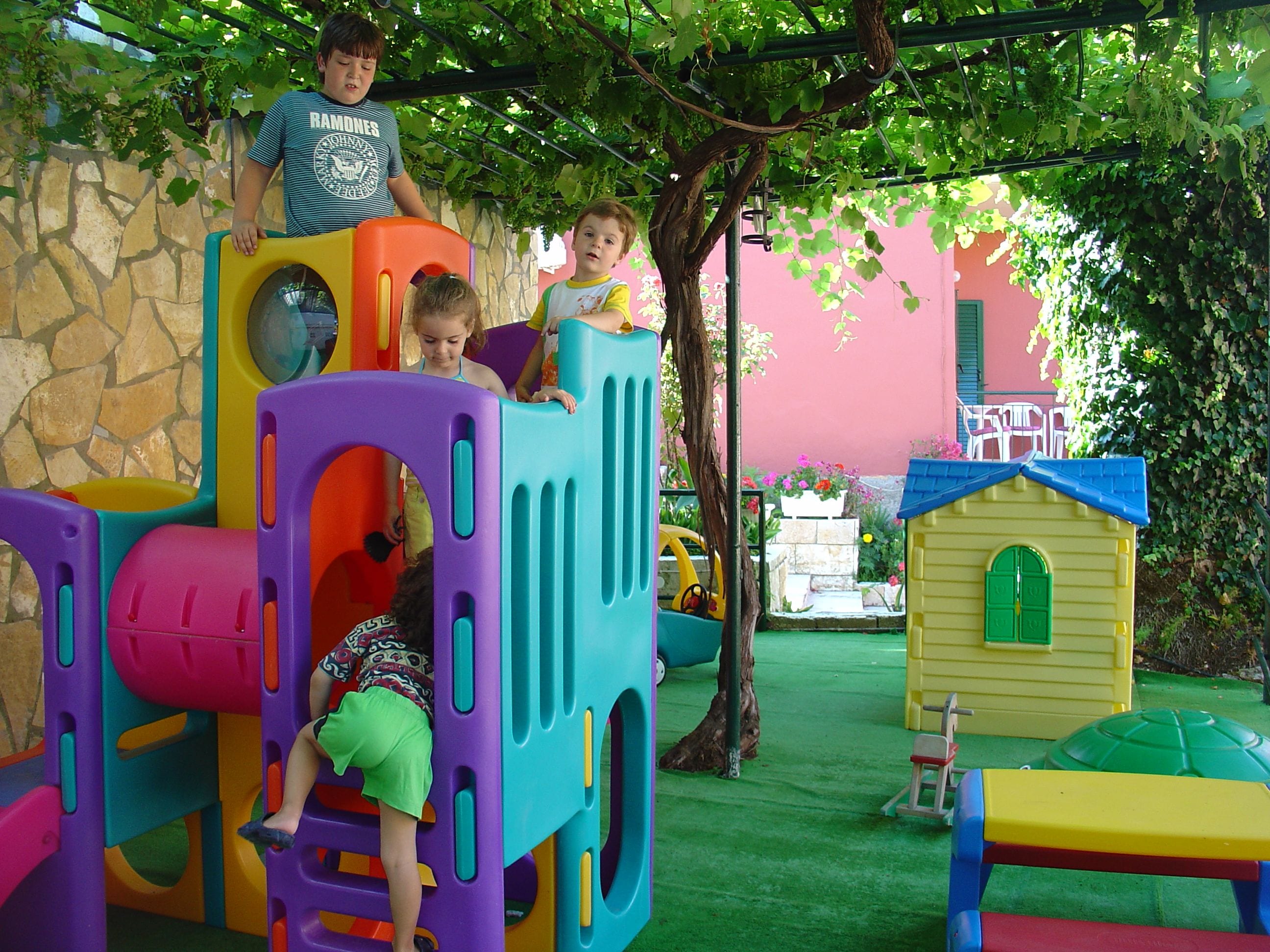 A children's play area with a colorful play structure, a small house, and a tree.