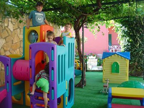 Un espace de jeux pour enfants avec une structure colorée, une petite maison et un arbre.
