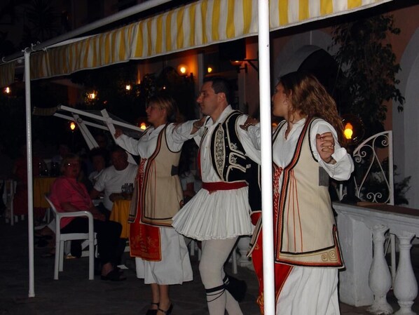 Un grupo de personas vestidas con atuendo tradicional bajo un toldo a rayas.