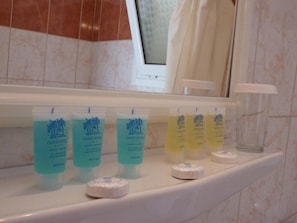 A bathroom with a marble wall, a window with a view, and toiletries on a shelf. - Oasis (Corfu)
