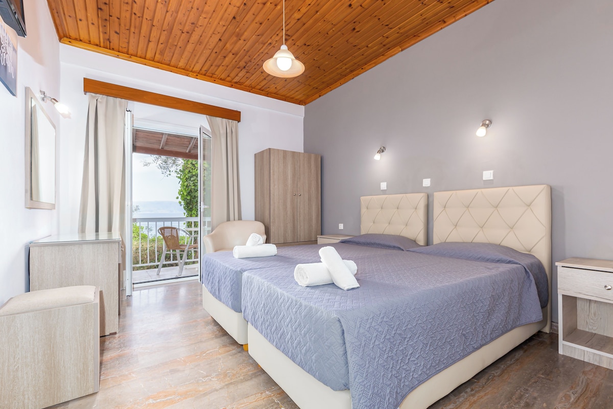 A bedroom with two beds, a wooden ceiling, and a balcony with a view.