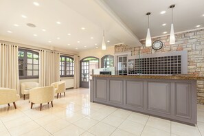 A modern reception area with a stone accent wall, a clock, and a counter with a glass display. - Oasis (Corfu)