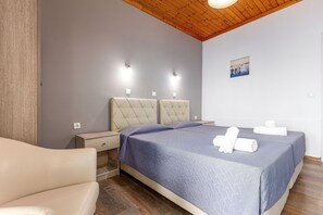 A bedroom with a bed, two bedside tables, a nightstand, a wooden ceiling, and a wall-mounted light fixture. - Oasis (Corfu)