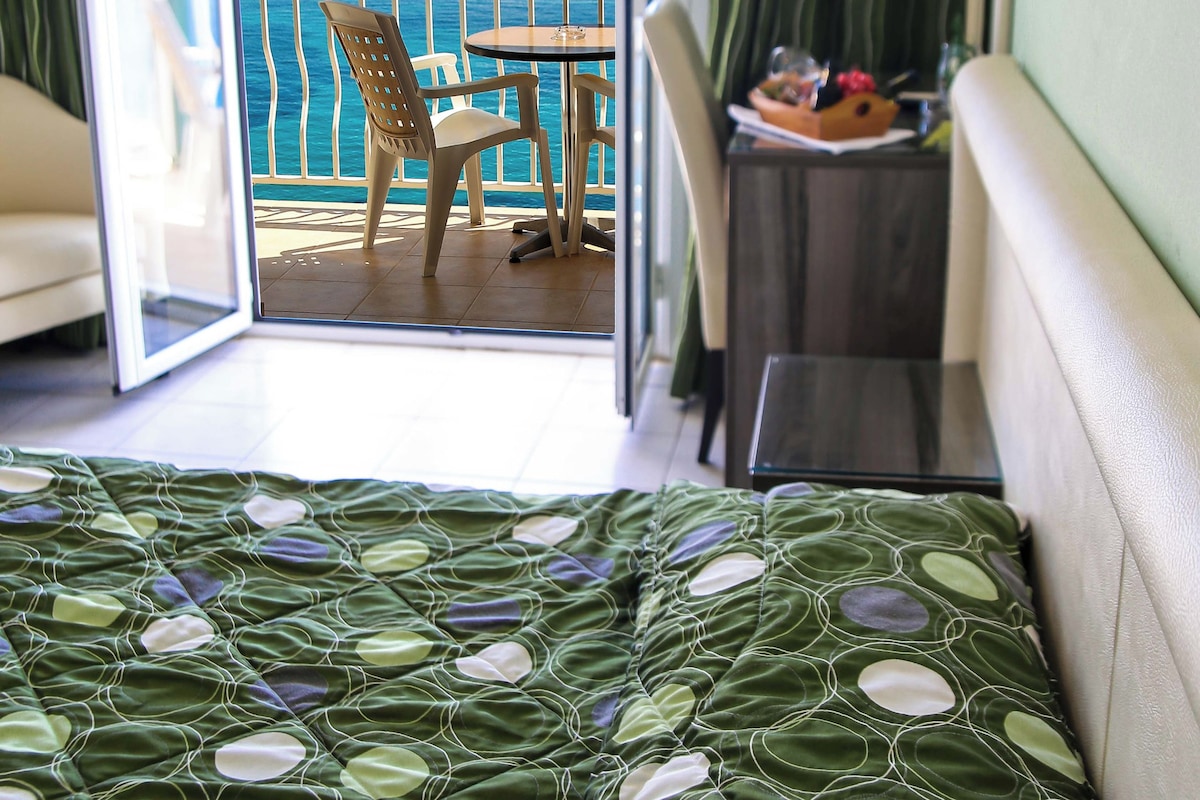 A hotel room with a bed, a chair, a table, and a view of the sea.