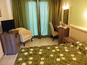 A hotel room with a bed, a desk, a chair, a television, and curtains.