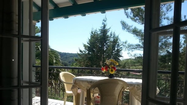 Ein Balkon mit Tisch und Stühlen, einer Blumenvase und Blick auf Bäume und Hügel.