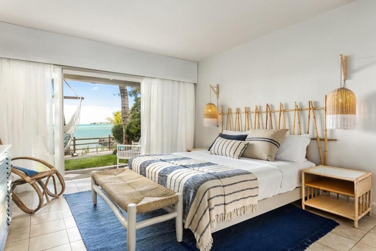 A bedroom with a bed, bedside tables, a bench, and a view of the ocean.