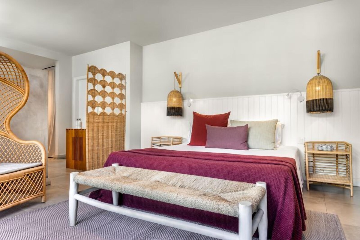 A modern bedroom with a large bed, a bench, wicker furniture, and decorative wall panels.