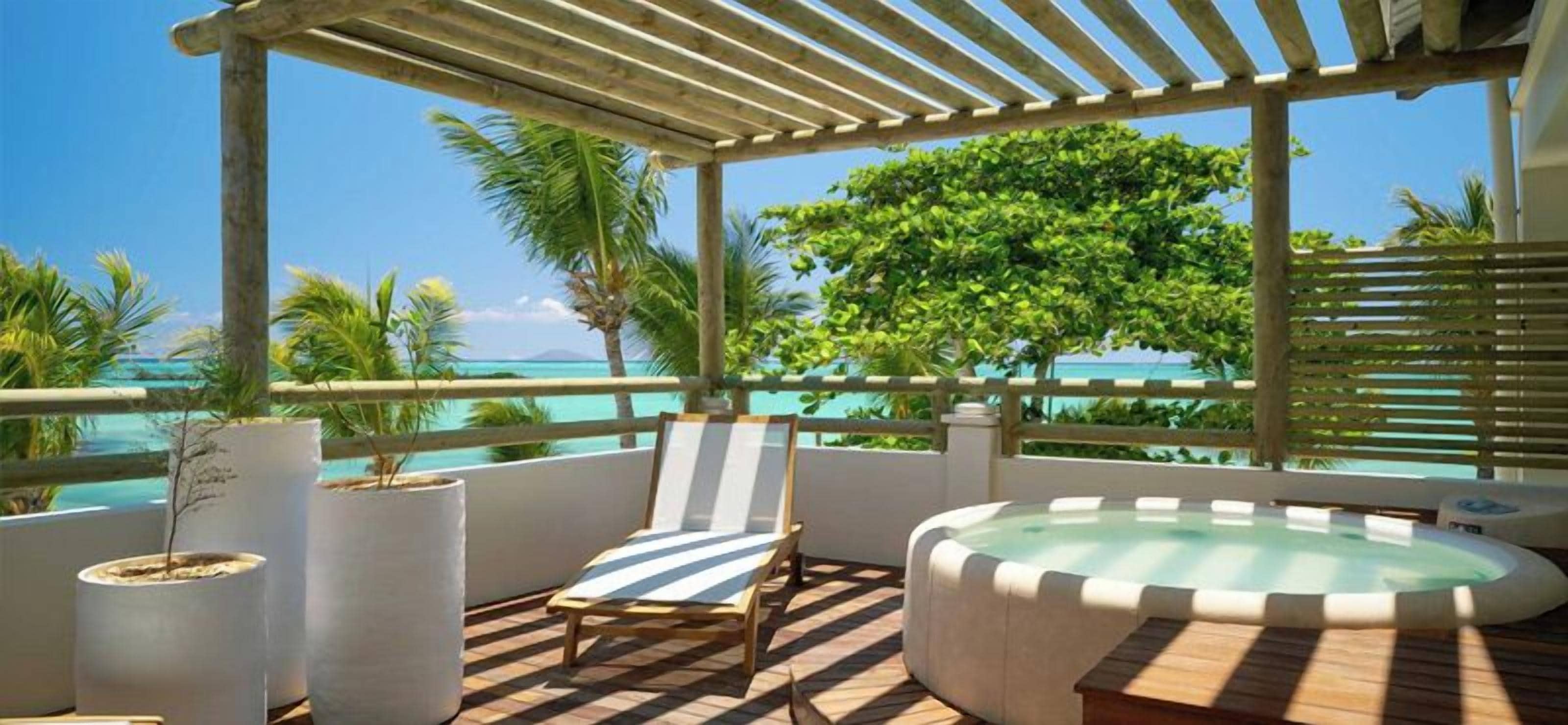 A covered outdoor area with a lounge chair, a hot tub, and potted plants.