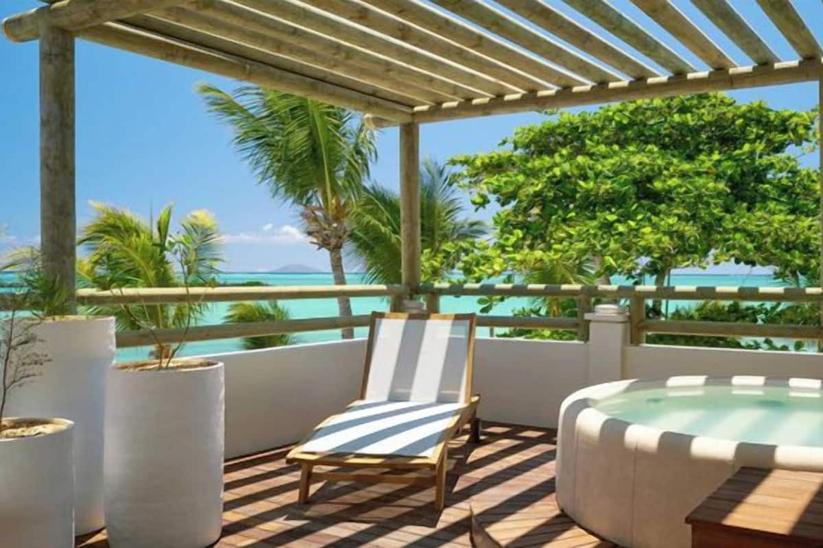 A covered outdoor area with a lounge chair, a hot tub, and potted plants.
