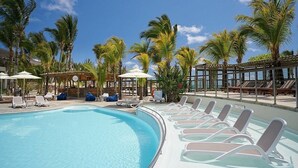 Un área de piscina con sillas de descanso, sombrillas y palmeras.