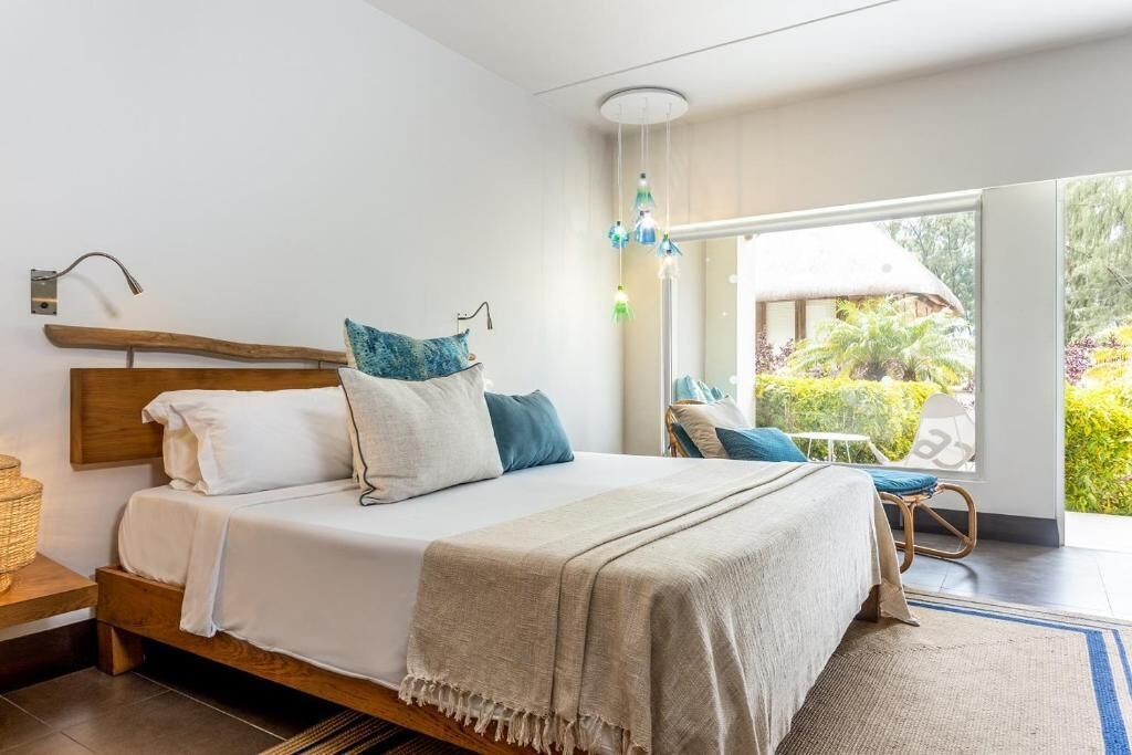 A bedroom with a bed, bedside tables, a window with a view of greenery, and a ceiling light fixture.