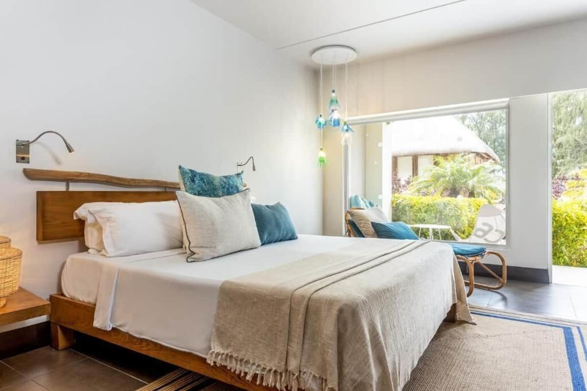 A bedroom with a wooden bed, white bedding, and a view of a garden through a large window.