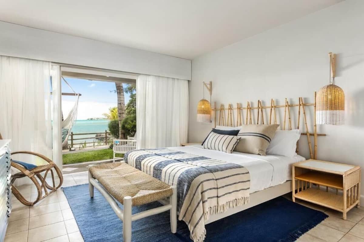 A bedroom with a bed, bedside tables, a bench, and a view of the ocean.