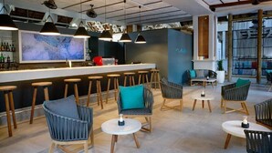 Un área de bar moderna con taburetes altos, sillas de mimbre y un cuadro abstracto grande en la pared.