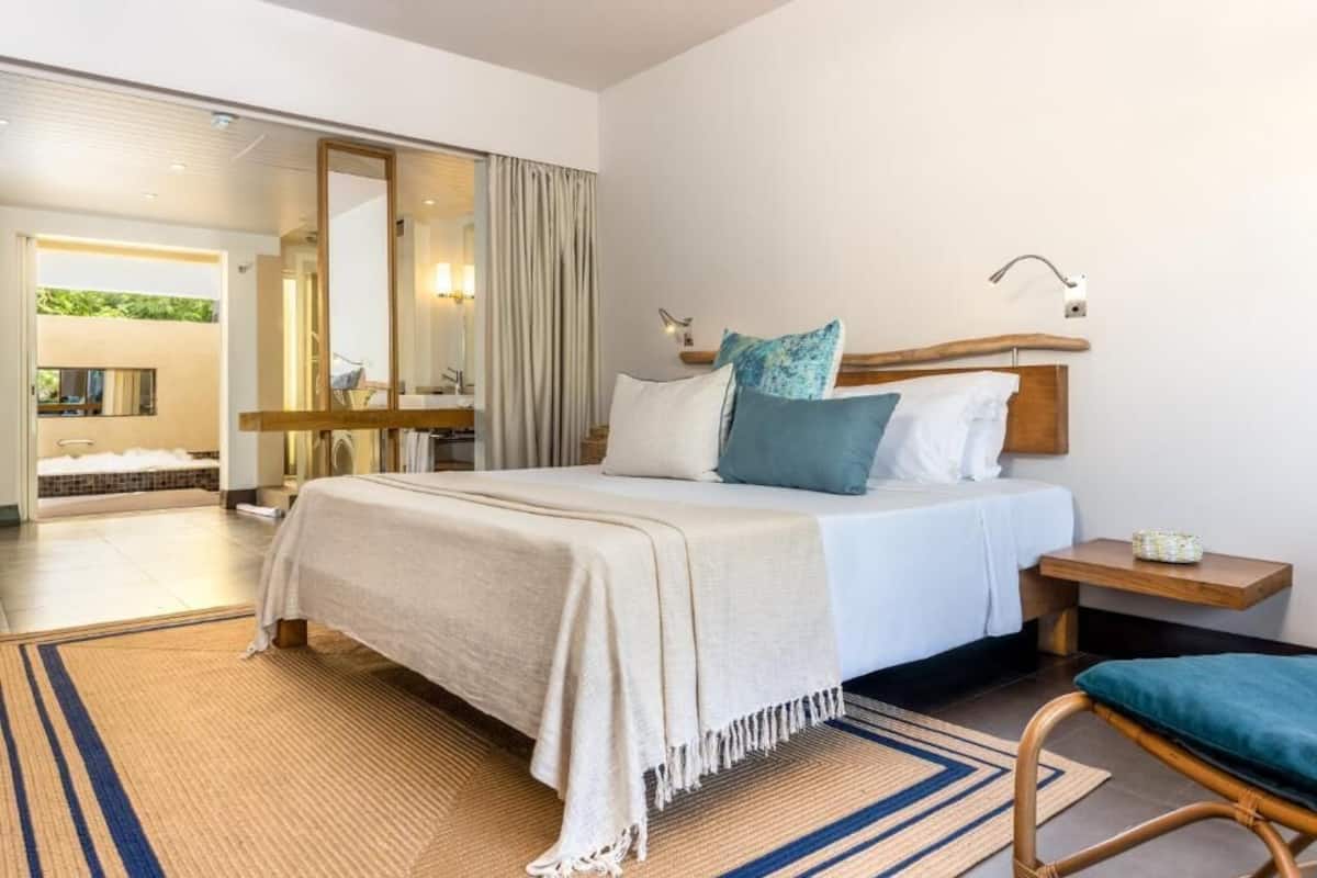 A modern hotel room with a large bed, a wooden headboard, a bedside table, and a view of a bathroom and outdoor area.