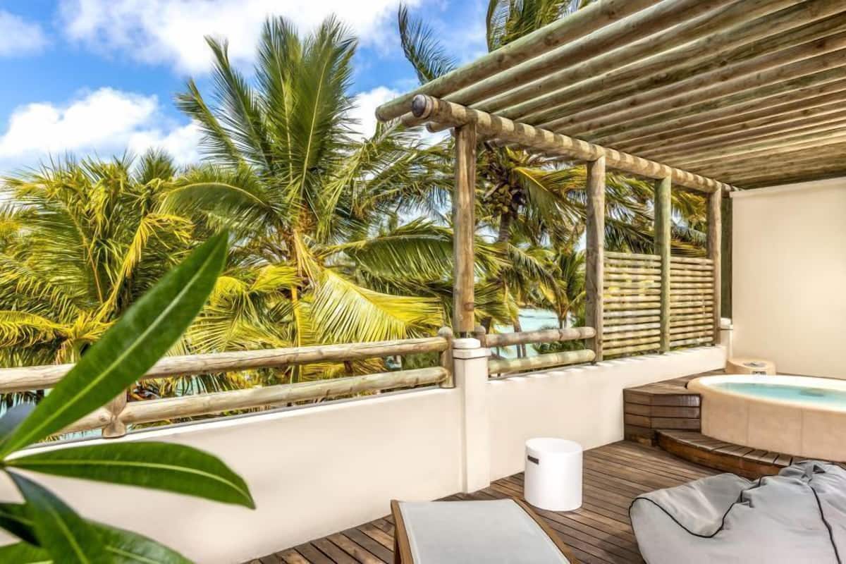 A wooden deck with a hot tub, palm trees, and a pergola.