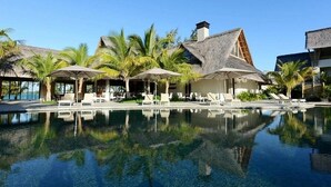 A resort with a clear pool, thatched-roof buildings, and palm trees.