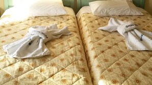 Two twin beds with floral bedding, white towels, and a painting on the wall. - Green Hill Studios & Apartments (Samos)