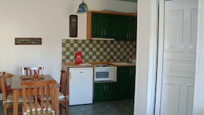 A compact kitchen with green cabinets, a white refrigerator, a microwave, and a dining table with chairs. - Green Hill Studios & Apartments (Samos)