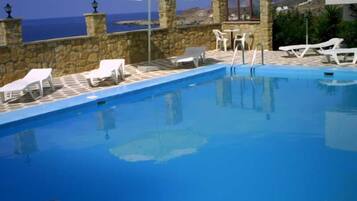Ein Pool mit Liegestühlen und Sonnenschirm, umgeben von Steinmauern und Blick auf das Meer.