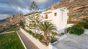 Ein Hotel namens 'Yiannis Hotel' mit heller Fassade, mehreren Balkonen und Blick auf eine gebirgige Landschaft.