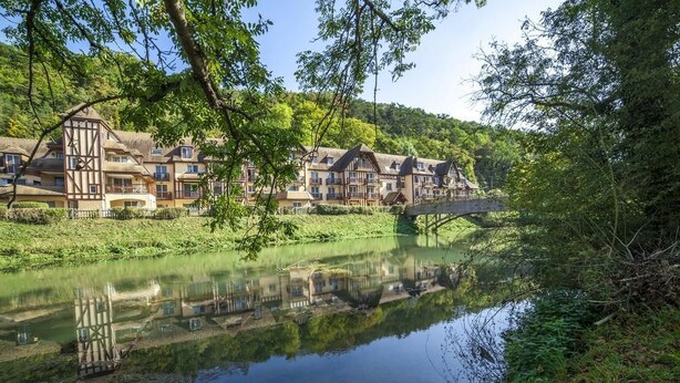 Un hôtel situé au bord d’un lac, doté d’une architecture traditionnelle, d’un pont et d’une végétation luxuriante.