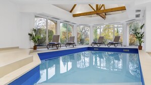 Une piscine intérieure moderne avec des parois en verre transparent, de nombreux fauteuils et des plantes en pot.