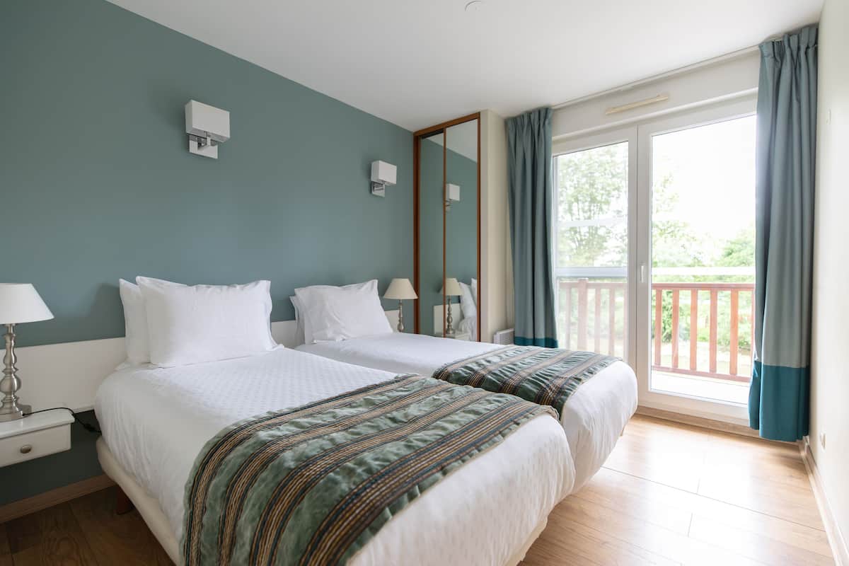 A hotel room with two beds, a balcony with a railing, and a large window with curtains.