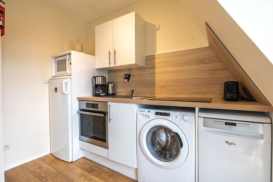 A compact kitchen with a microwave, coffee maker, oven, and washing machine.