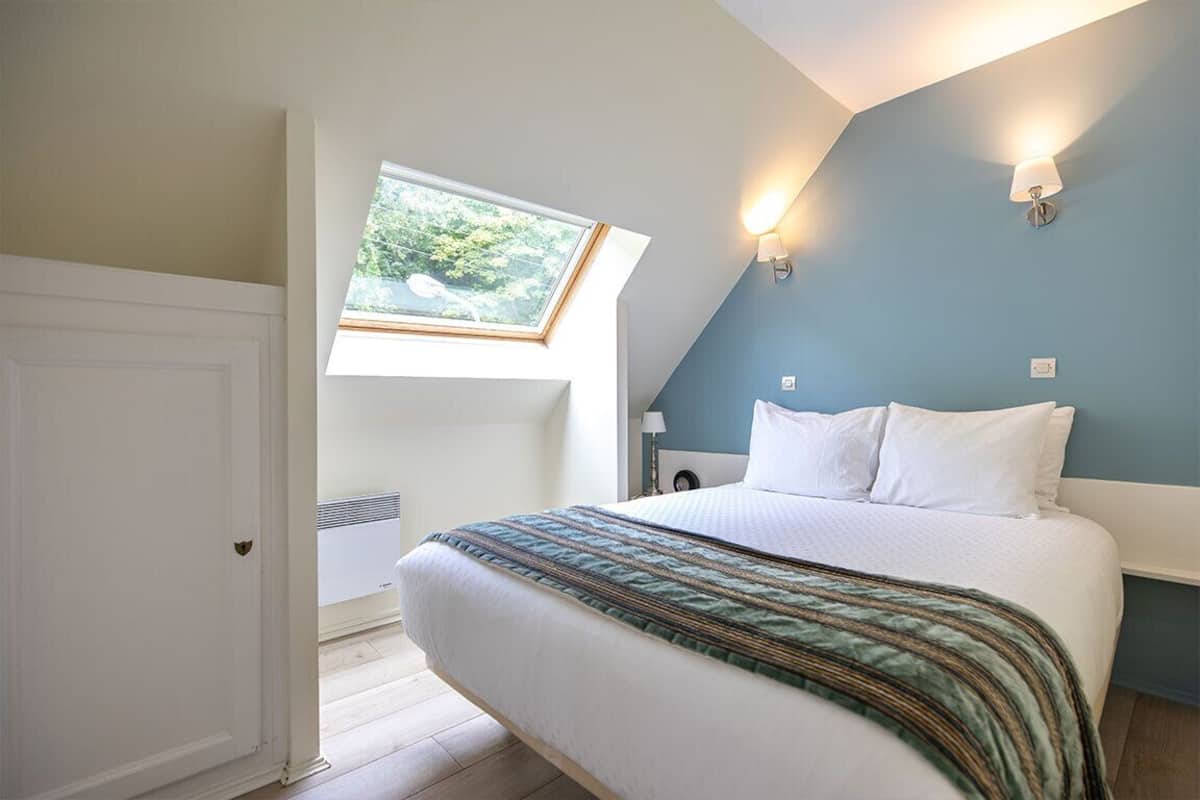 A bedroom with a bed, a skylight, and a wall-mounted light fixture.