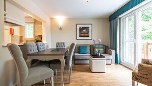 Un salon moderne comprenant une table à manger, des chaises recouvertes d’un tissu gris, un canapé gris, un pouf blanc et un tableau encadré accroché au mur.