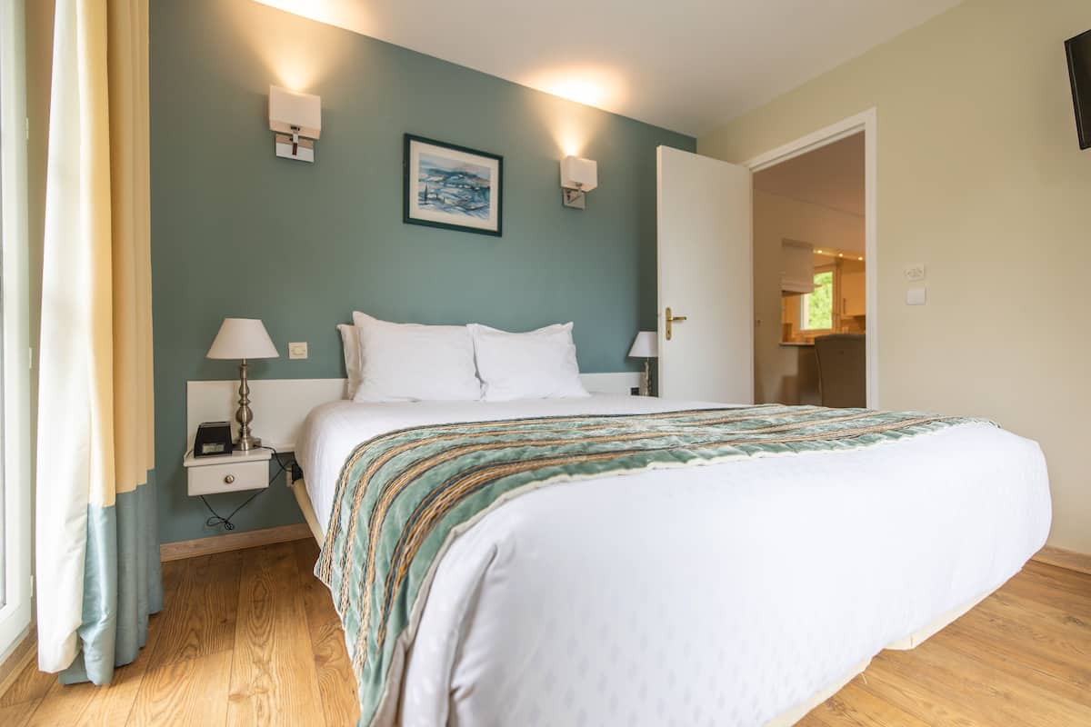 A neatly made bed with white linens, a bedside table with a lamp, and a wall-mounted picture.