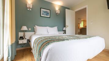 A neatly made bed with white linens, a bedside table with a lamp, and a wall-mounted picture.