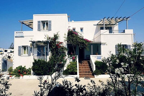 Un bâtiment blanc avec une enseigne indiquant « KYMATA ROOMS SEDIOS » et un escalier menant à l’entrée.