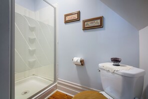 Bathroom features a glass shower enclosure, framed pictures, and a decorative bowl on the toilet tank.