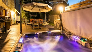 A hot tub with colorful LED lights, an umbrella, and outdoor furniture in a backyard setting. - Les Matins de Victoria (Waterloo)