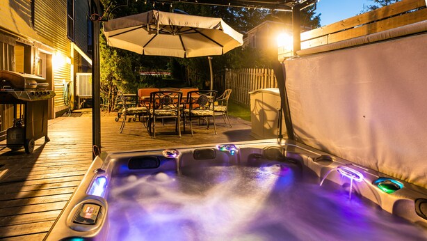 A hot tub with colorful LED lights, an umbrella, and outdoor furniture in a backyard setting. - Les Matins de Victoria (Waterloo)
