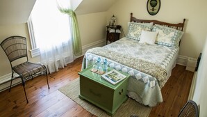 A bedroom with a wooden bed, a green nightstand, a wicker chair, and a window with curtains. - Les Matins de Victoria (Waterloo)