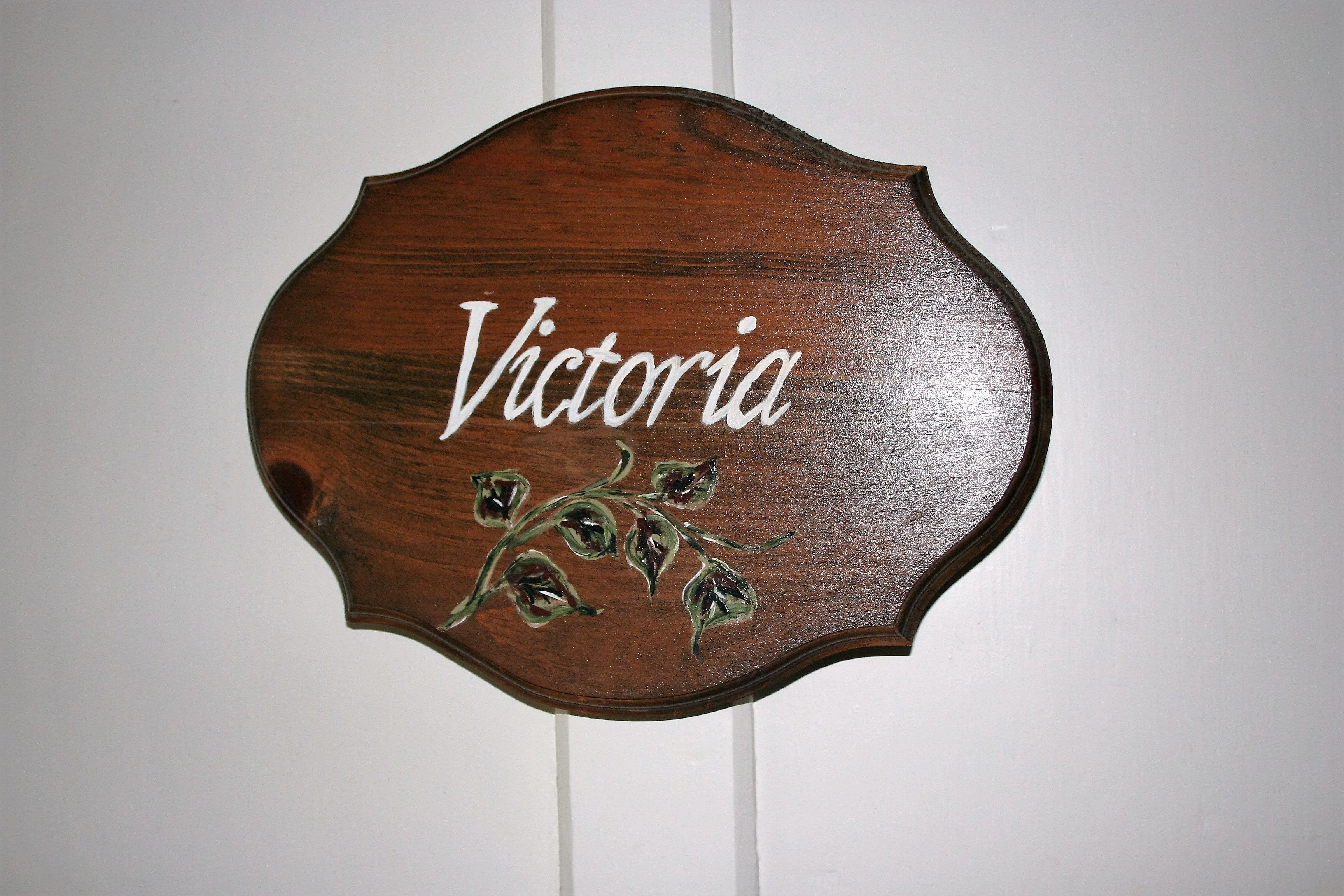 Ein Holzschild mit dem Schriftzug "Victoria" und floralem Dekor.