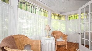 A sunlit room with wicker chairs, a small table with a lamp, and a door with glass panels. - Les Matins de Victoria (Waterloo)