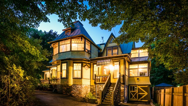 A large, multi-story house with a prominent front porch and a staircase leading to the upper floor. - Les Matins de Victoria (Waterloo)