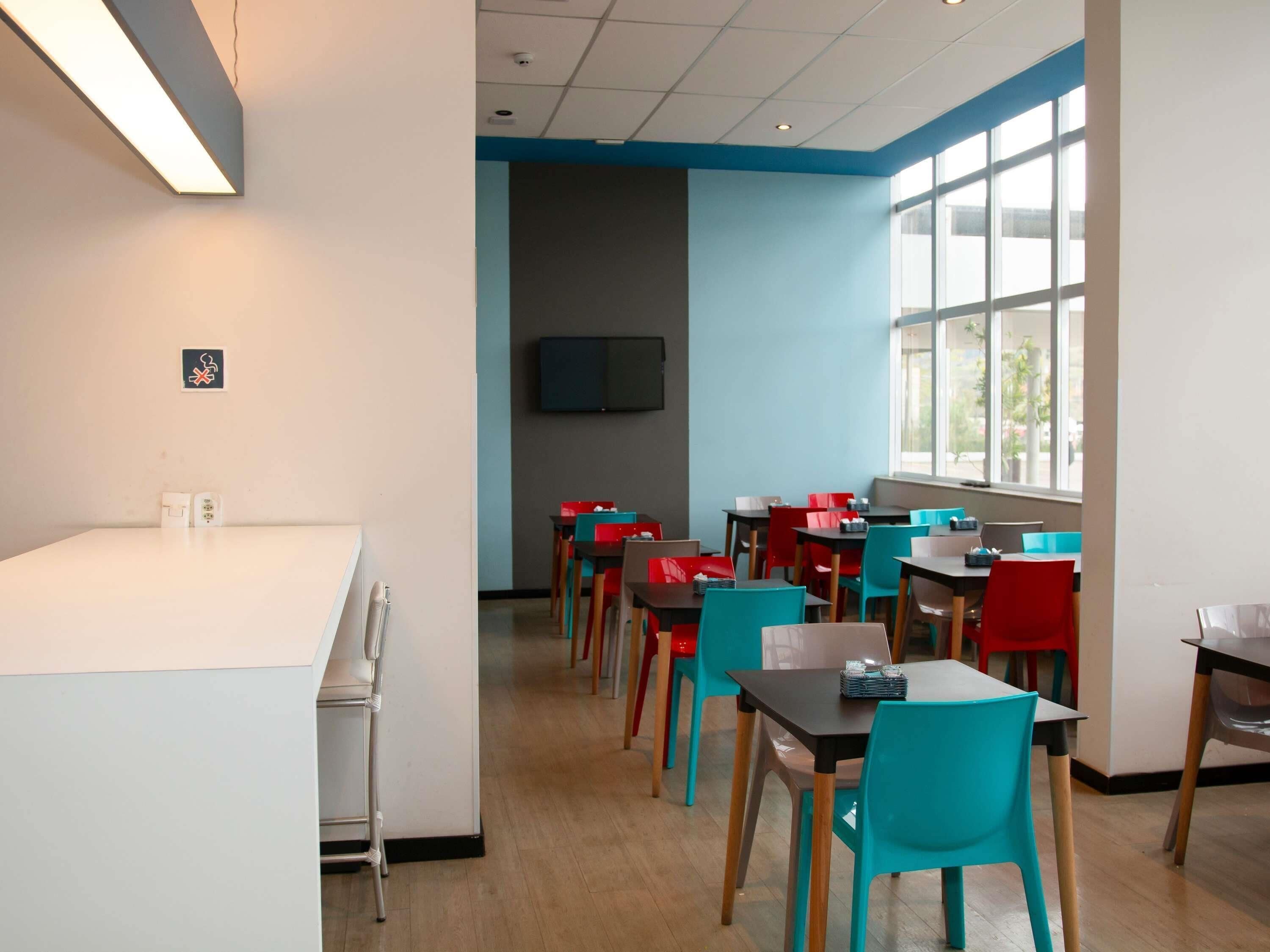 Un comedor moderno con una encimera blanca, sillas coloridas y un amplio ventanal que ofrece luz natural.