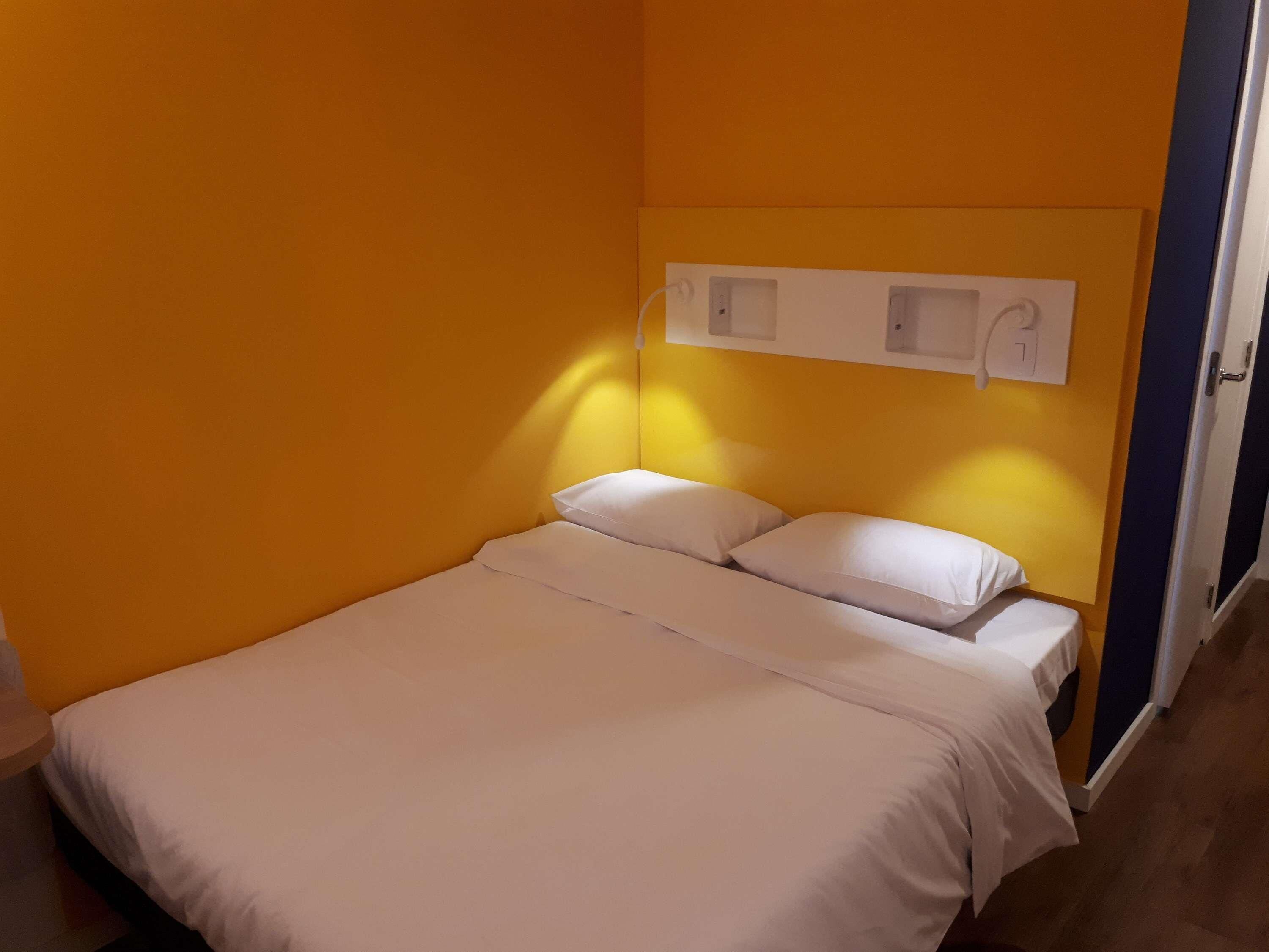 A single bed with white bedding in a room with yellow walls and a door to the right.
